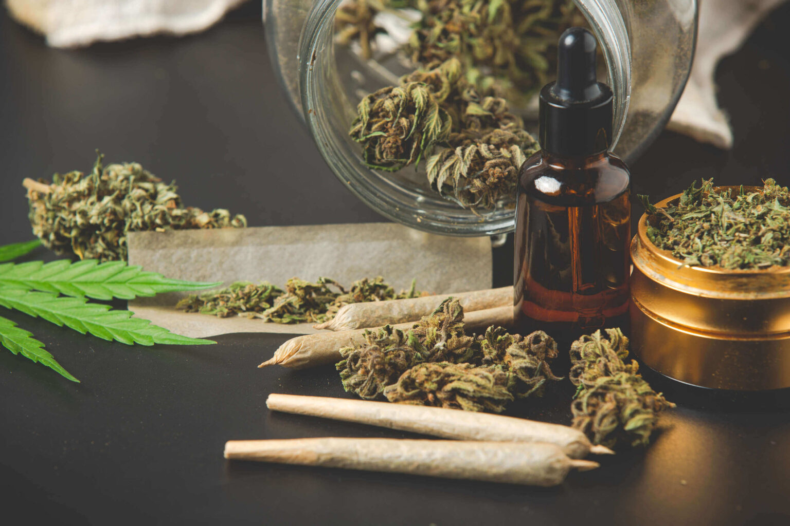 Nature's Canopy House A display of cannabis products from Natures Canopy House on a table, including rolled joints, a dropper bottle, a grinder with ground cannabis, and a glass jar with cannabis buds. A cannabis leaf is also visible. Dispensary In Mississauga