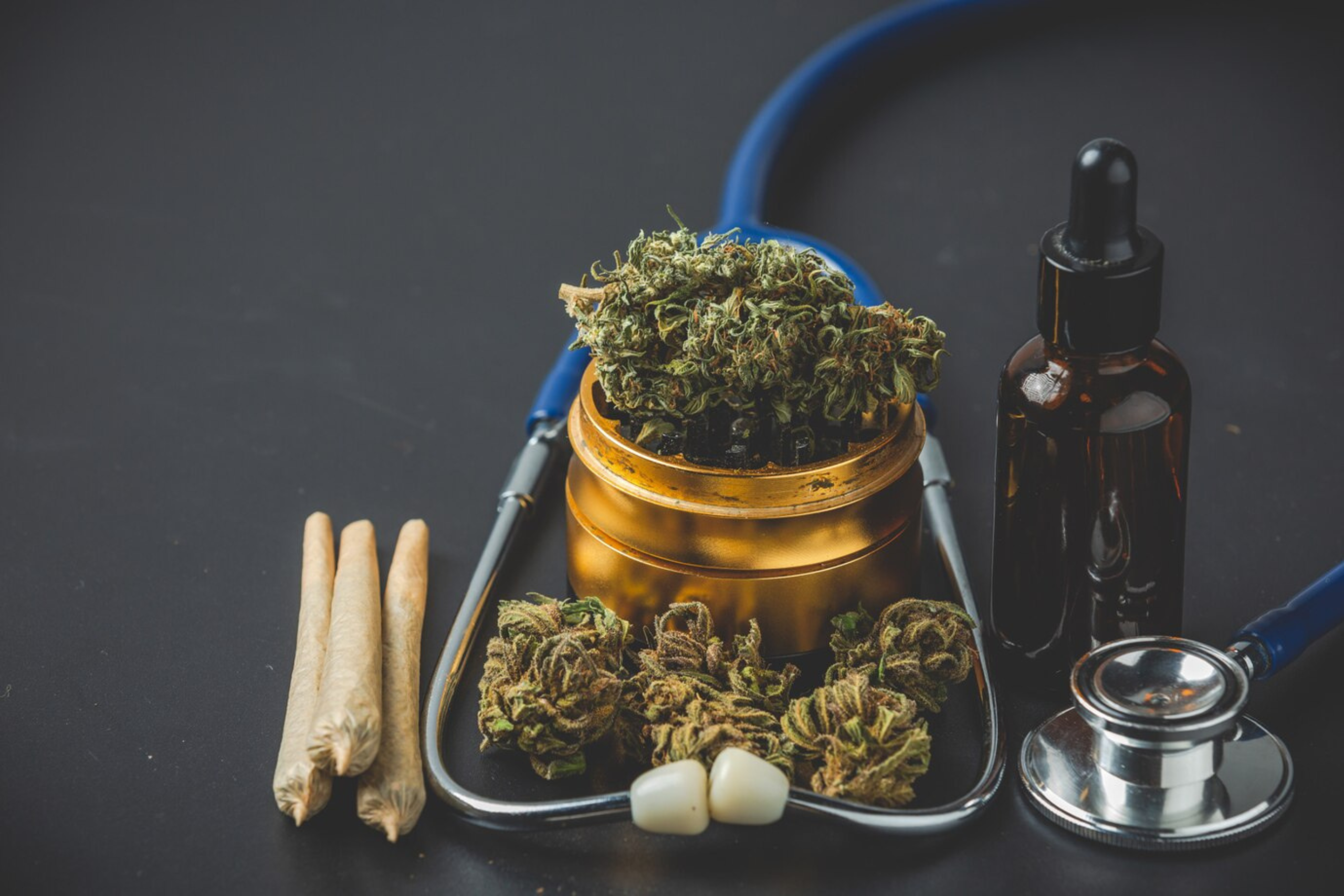 Nature's Canopy House A stethoscope is placed around a container of cannabis buds, with rolled joints, a dropper bottle, and loose buds on a dark background—an intriguing scene at Nature's Canopy House. Dispensary In Mississauga