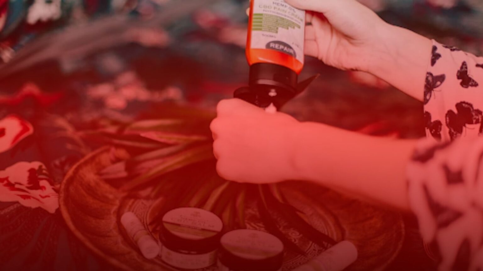 Nature's Canopy House Person applying a cream from an orange bottle onto their hand over a table with various cosmetic products in Natures Canopy House. Dispensary In Mississauga