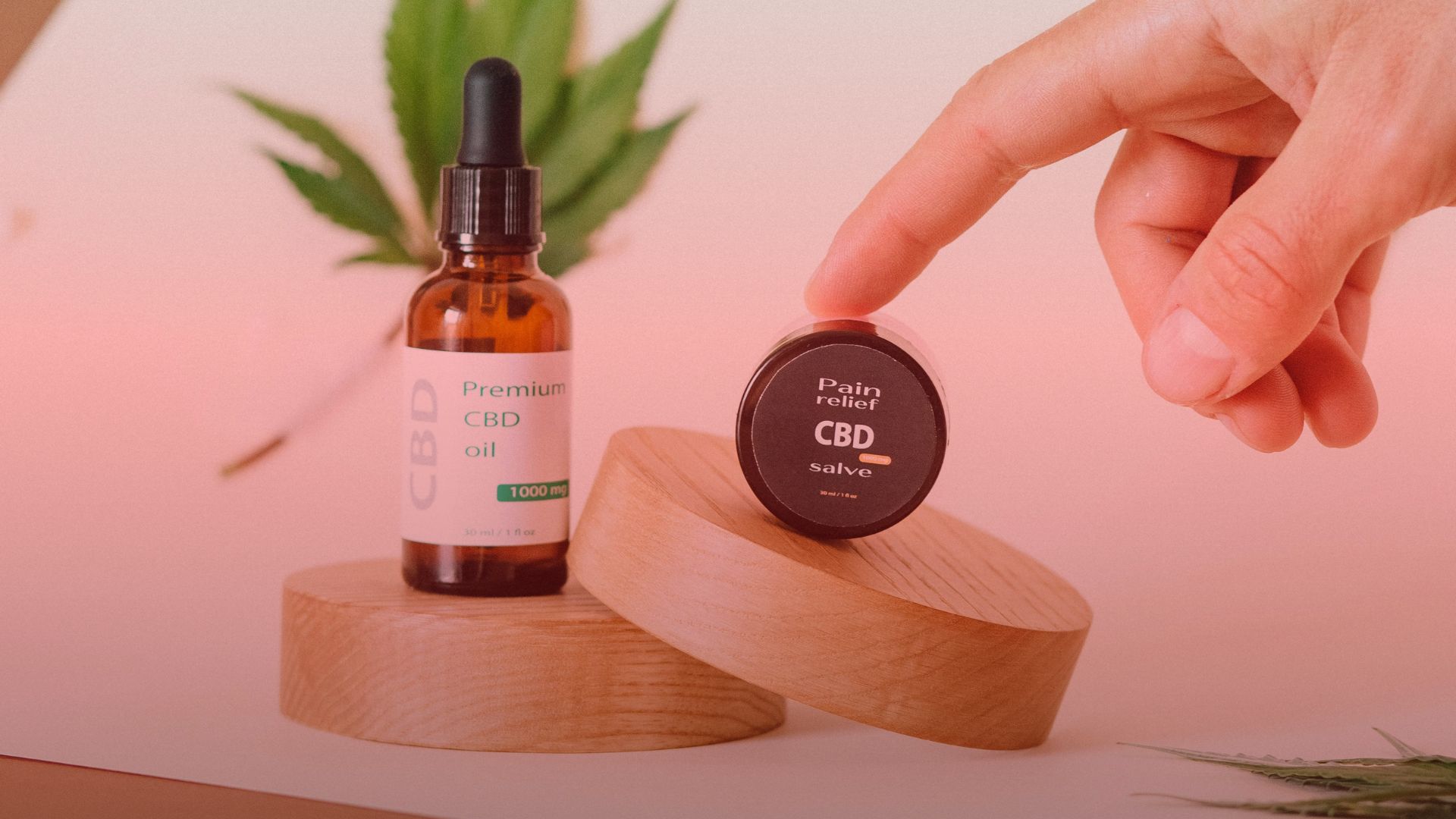 Nature's Canopy House Hand reaching for a CBD salve on a wooden stand next to a bottle of Premium CBD oil, with a leaf in the background. Dispensary In East York and York