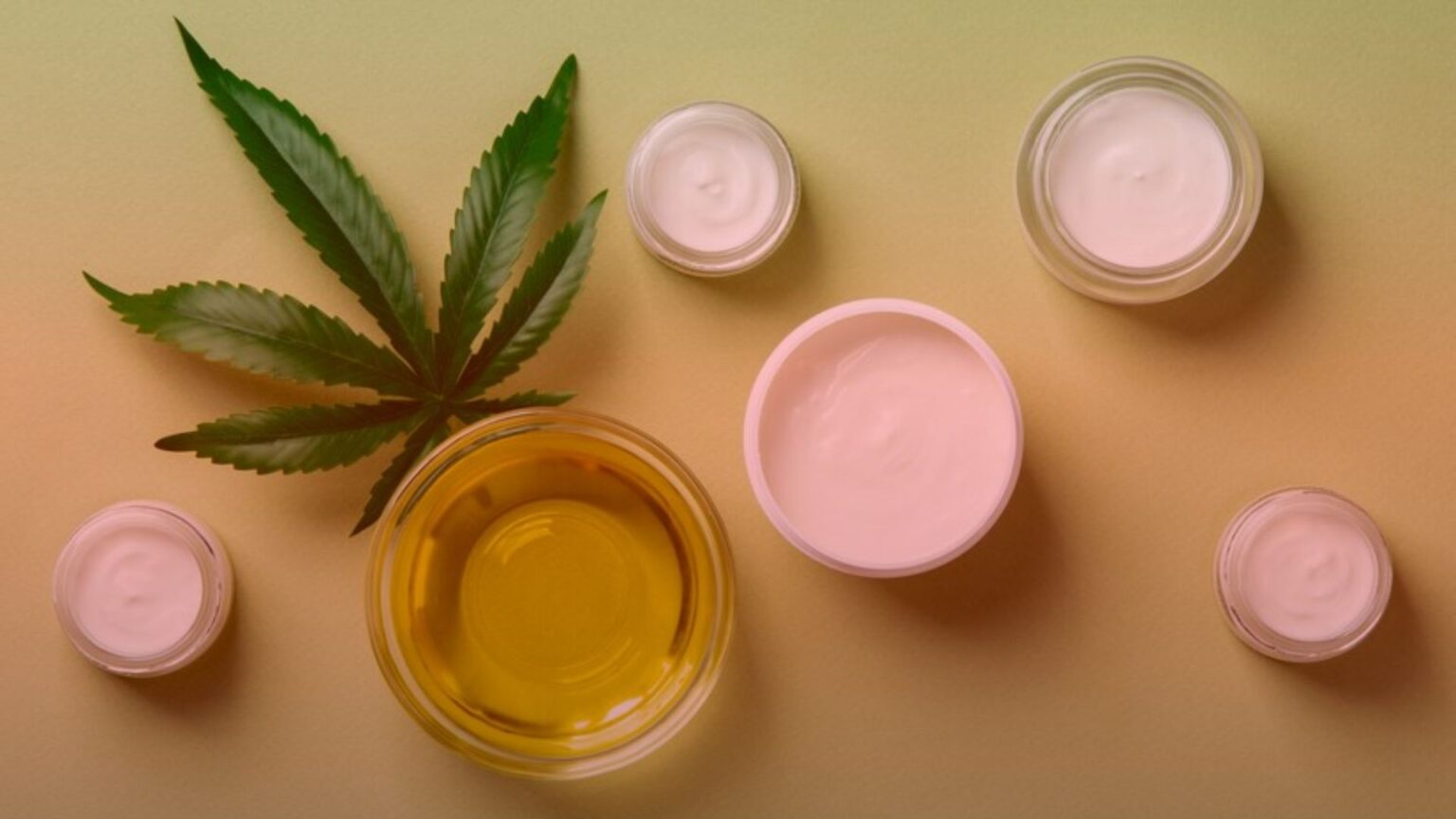 Nature's Canopy House Various jars of cream and a bowl of oil are arranged next to a cannabis leaf on a yellow background, all available at Natures Canopy House. Dispensary In Mississauga