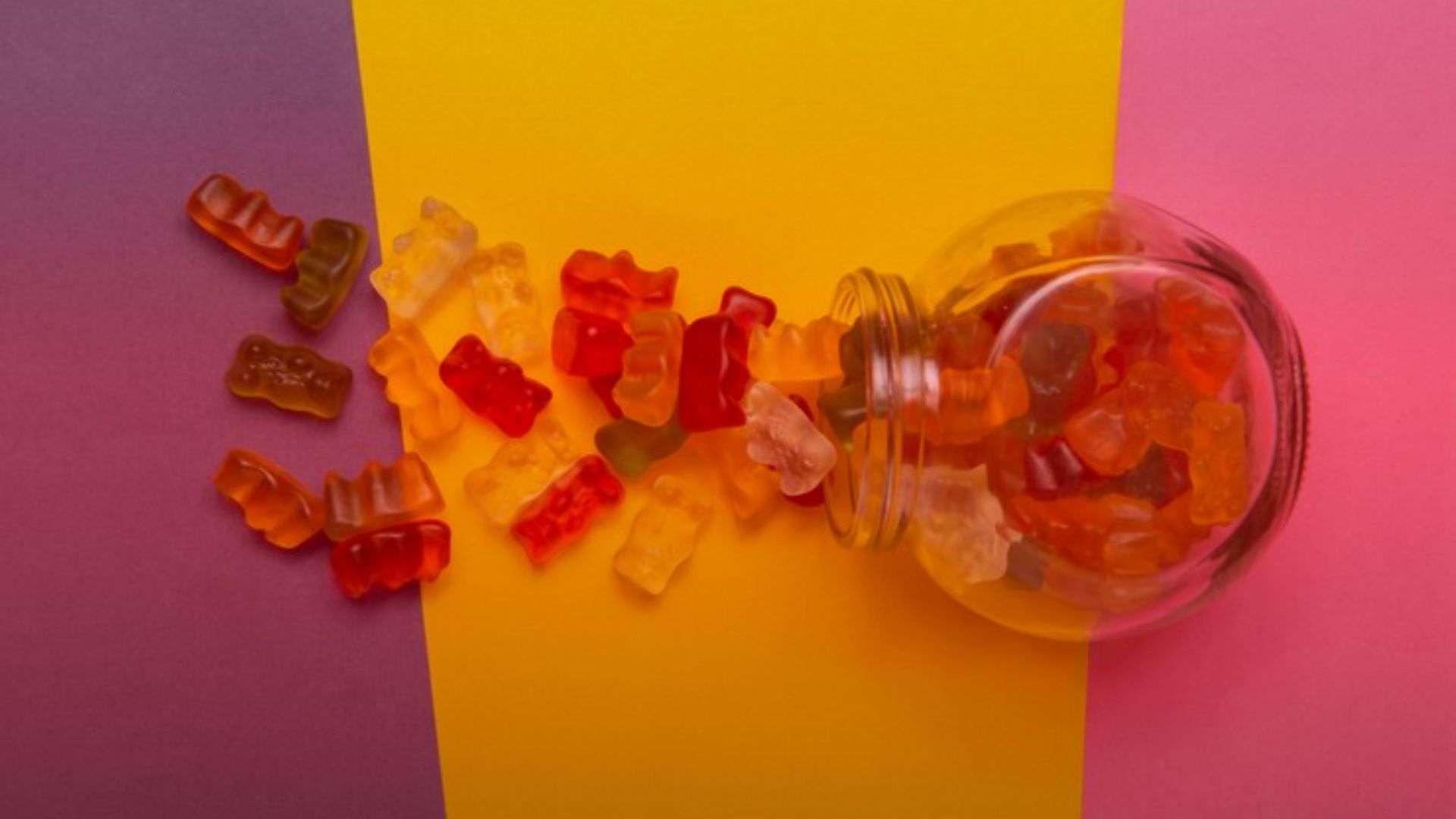 Nature's Canopy House A jar of tipped over, spilling colorful gummy bears onto a purple, yellow, and pink background. Dispensary In Mississauga