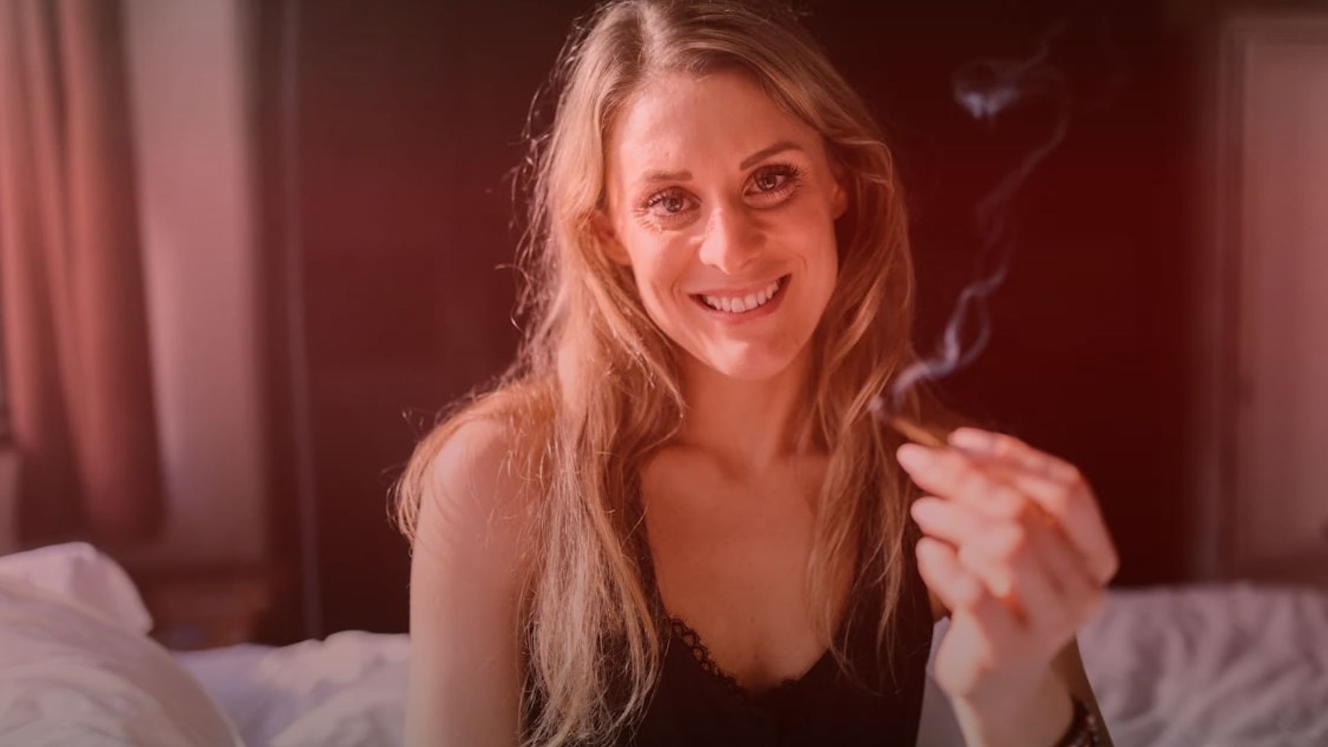 Nature's Canopy House A woman sits on a bed, smiling and holding a cannabis cigarette with smoke rising, savoring the moment. Her relaxed demeanor is a testament to the positive impact of cannabis experiences. Dispensary In Mississauga