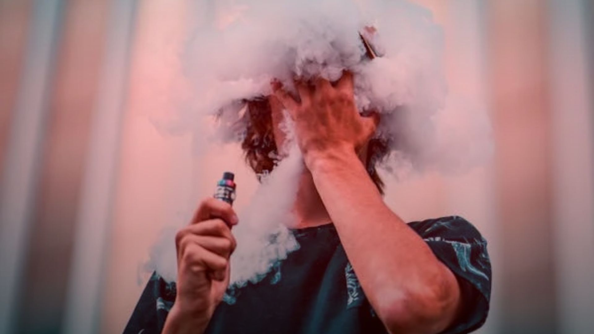 Nature's Canopy House A person holding a nicotine vape device releases a dense cloud of vapor, obscuring their face. The background features vertical lines in warm tones. Dispensary In Mississauga