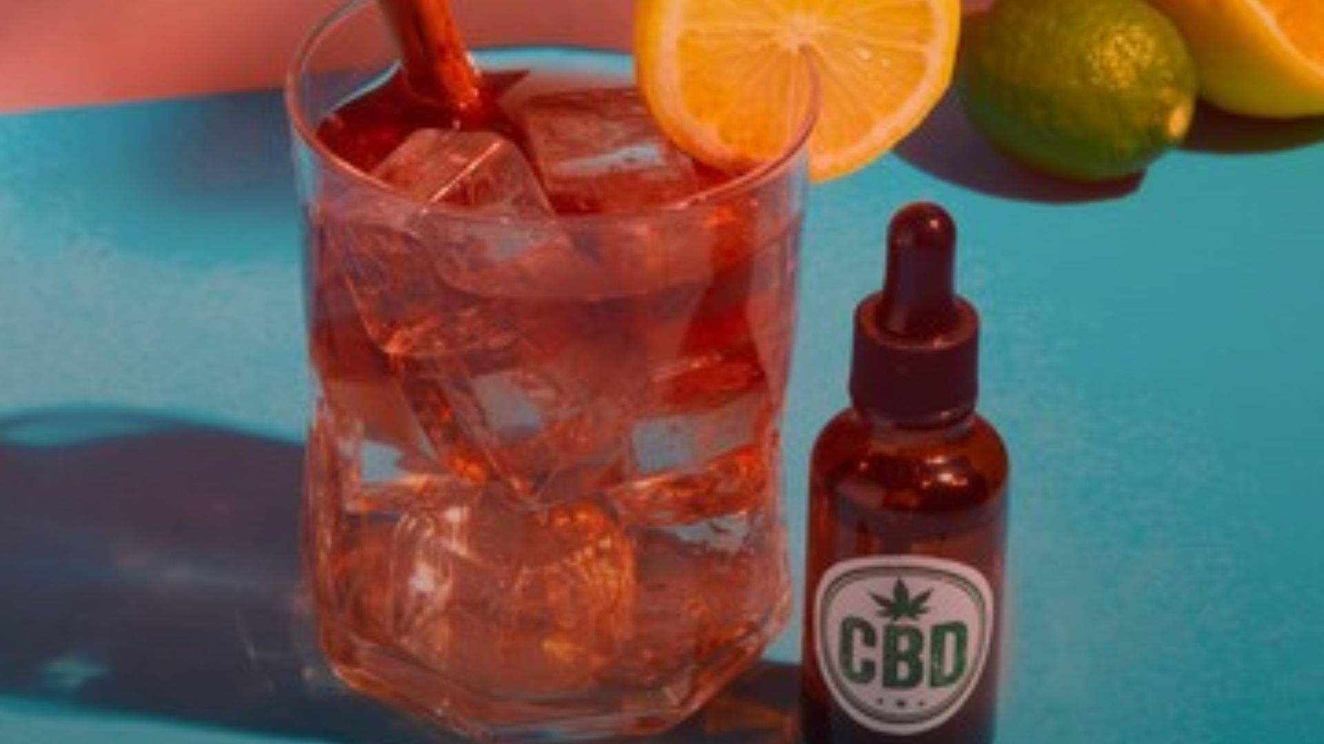 Nature's Canopy House A glass of iced cannabis beverage with a lemon slice and a brown dropper bottle labeled "CBD" sits on a blue surface, surrounded by fresh lemons and limes, offering a refreshing twist. Dispensary In Mississauga