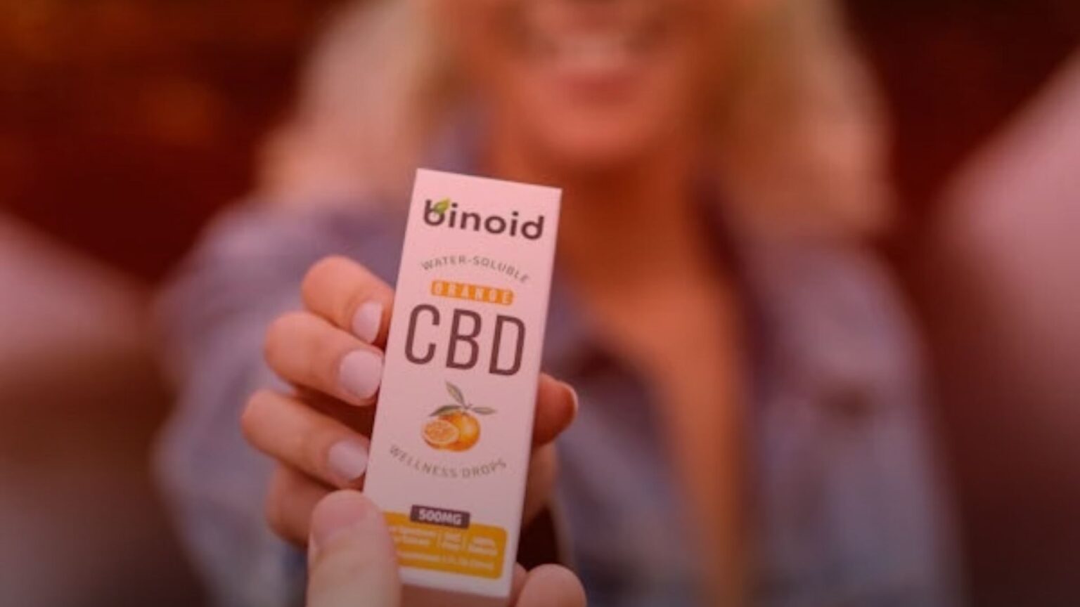 Nature's Canopy House A person holds a box of Binoid water-soluble CBD wellness drops with 500mg orange flavor in focus, a popular choice in Cannabis Stores Mississauga. Dispensary In Mississauga