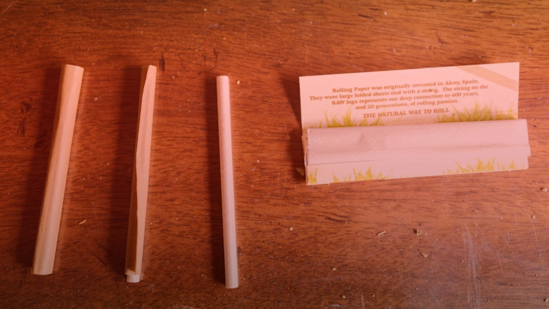 Nature's Canopy House Three rolled paper tubes sit on a wooden surface, accompanied by rolling paper and a rolling machine on the right—an ideal setup for those considering organized pre-roll storage solutions. Dispensary In Mississauga